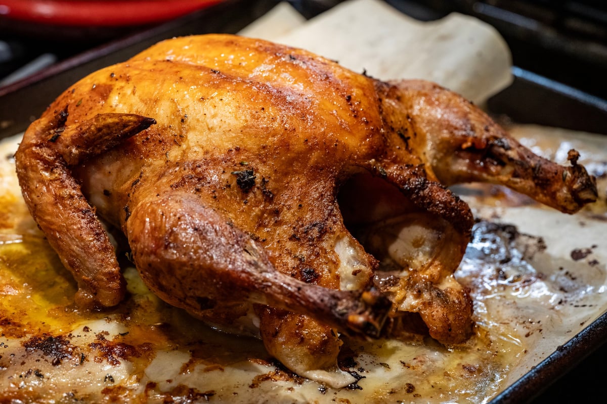 A whole chicken marinated after being roasted, in a serving dish