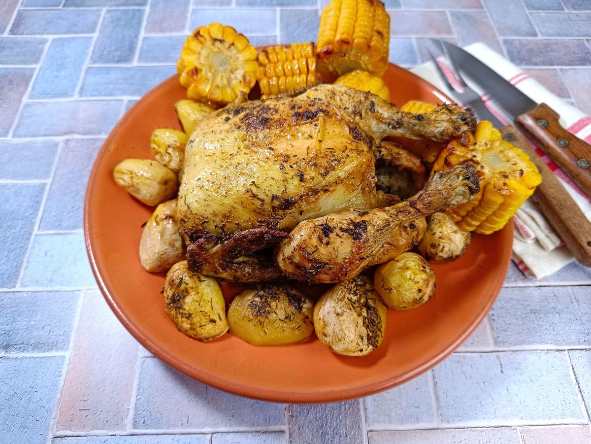 A roast chicken served with potatoes and grilled corn